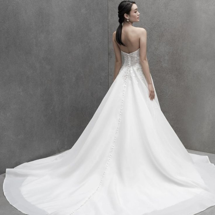 a woman in a white wedding dress is standing against a wall and looking off into the distance