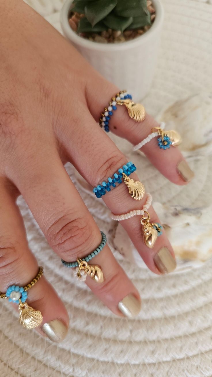 a woman's hand with gold and blue nail polishes on her nails next to a potted plant