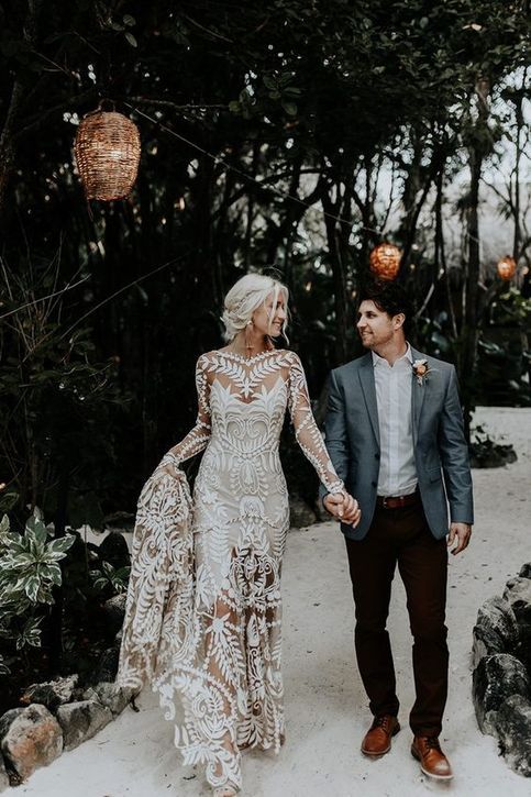 a bride and groom holding hands walking through the woods