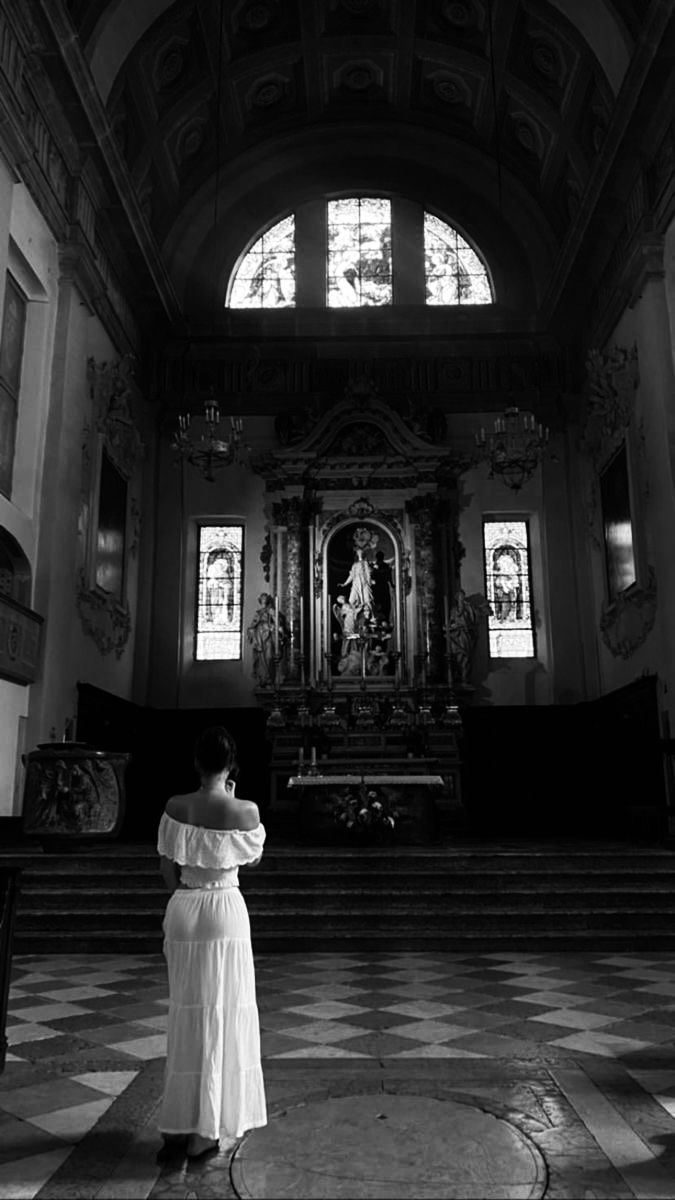 a woman in a white dress standing at the end of a church aisle with stained glass windows