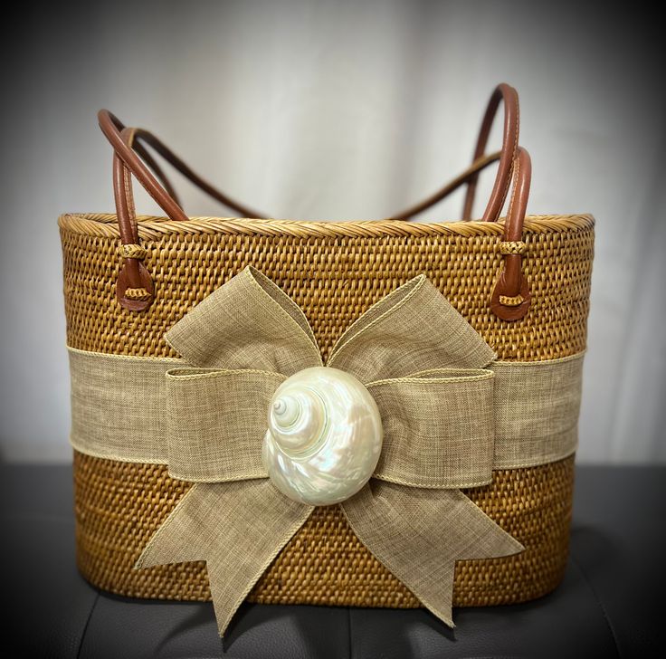 a wicker basket with a large bow on the side and a pearl in the center