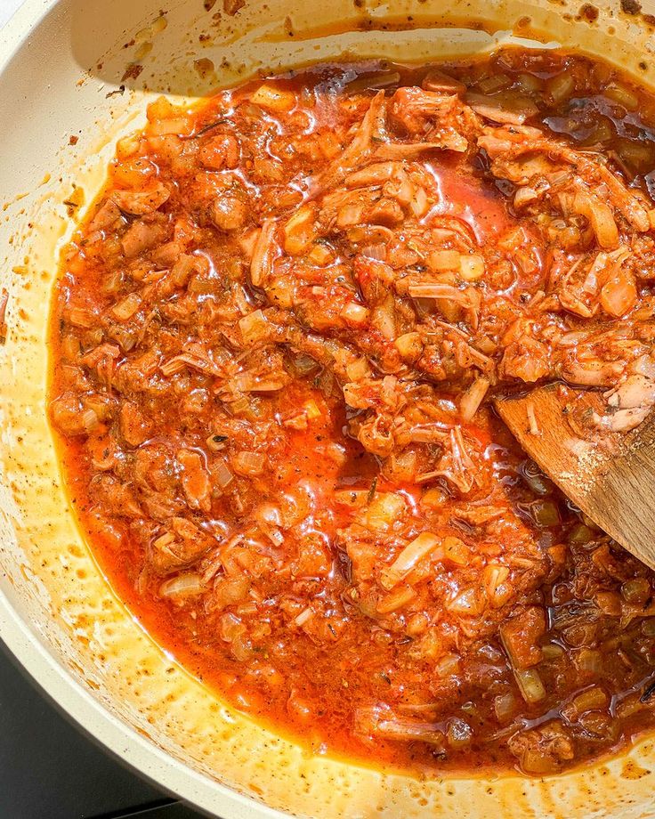 a pot filled with meat and sauce being stirred by a wooden spoon on the stove