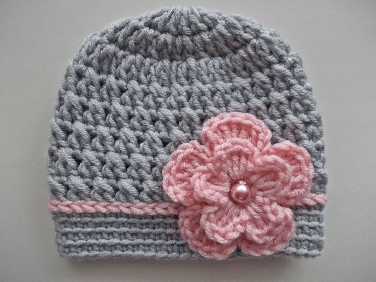 a crocheted hat with a pink flower on the front and gray side, sitting on top of a table