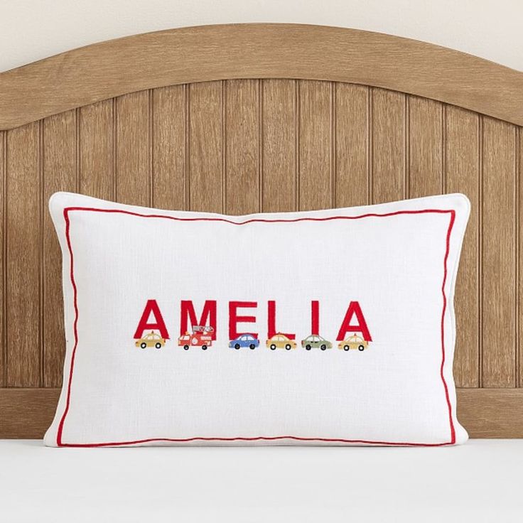 a white pillow with the word amella on it in red stitching and trucks