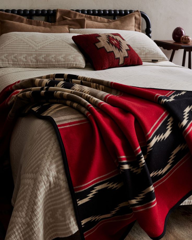 a bed covered in blankets and pillows next to a night stand