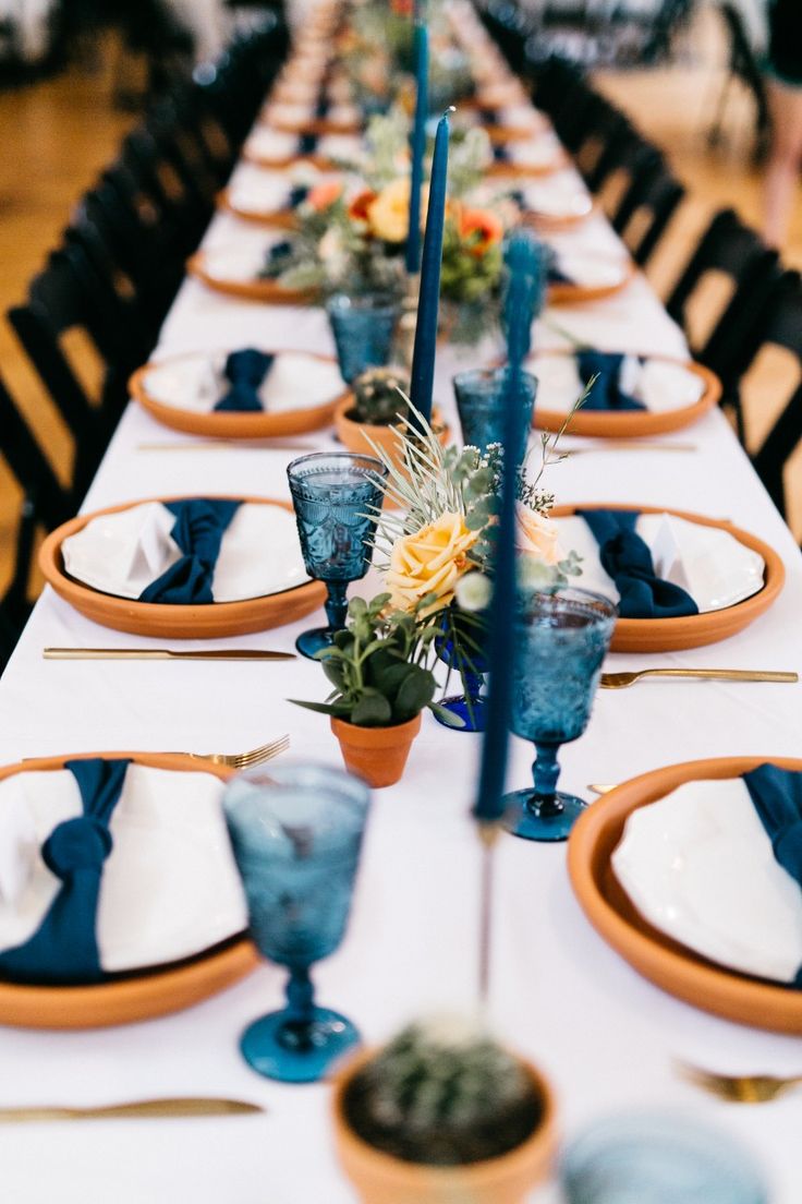 the table is set with blue and white dishes, candles, and flowers in vases