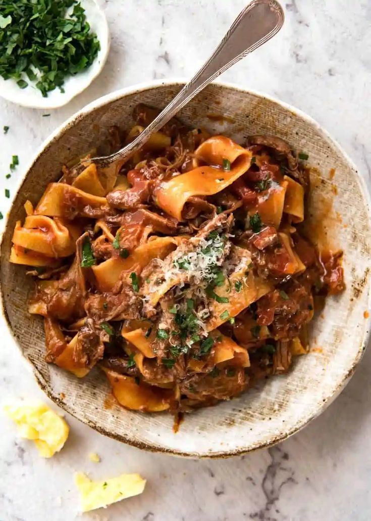 a bowl full of pasta with meat and parmesan cheese on the side next to garlic