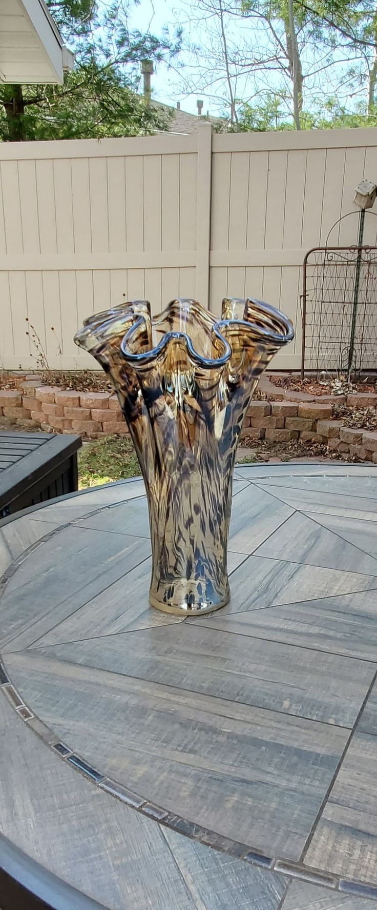 a glass vase sitting on top of a wooden table in the middle of a yard