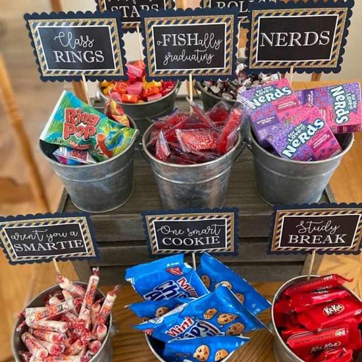 an assortment of candy in buckets on a table with signs and place card holders