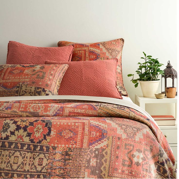 a bed with an orange and red comforter on top of it next to a potted plant