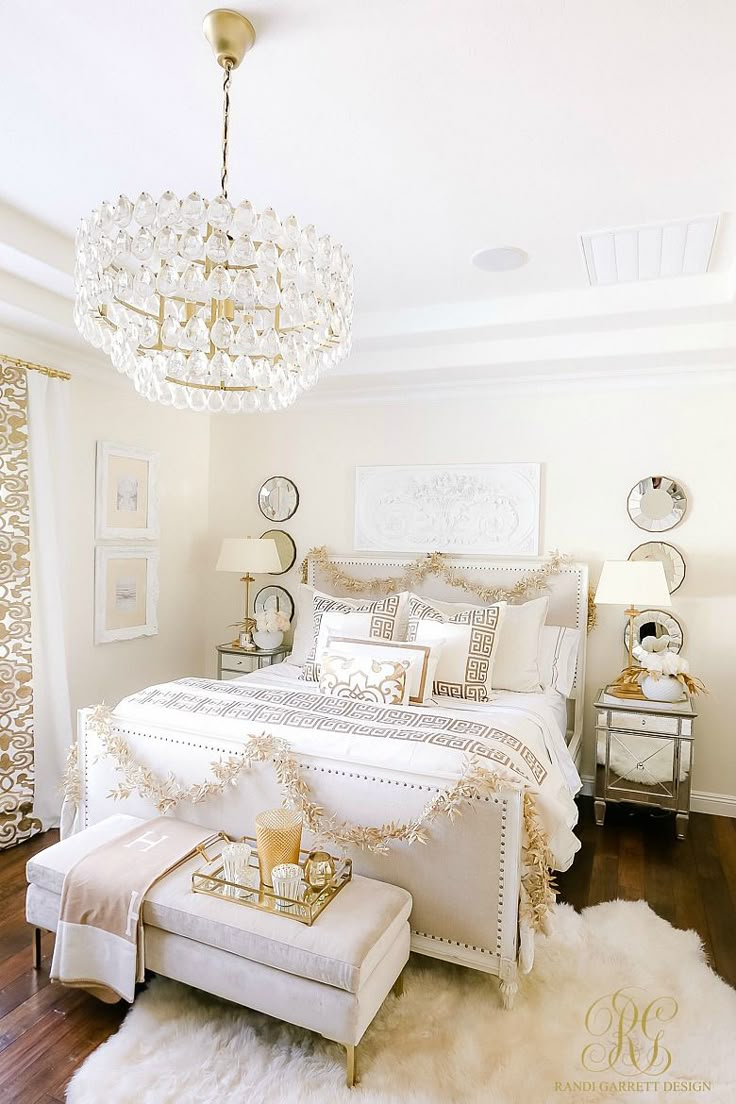 a white bedroom with a chandelier hanging from the ceiling and pillows on the bed