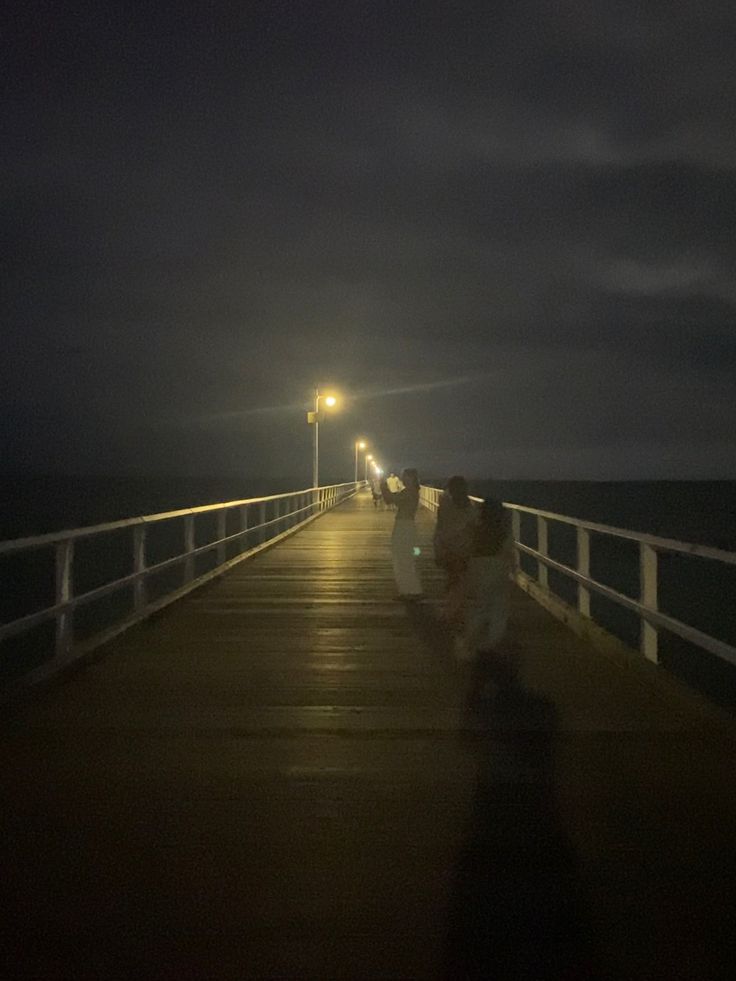 two people walking down a pier at night