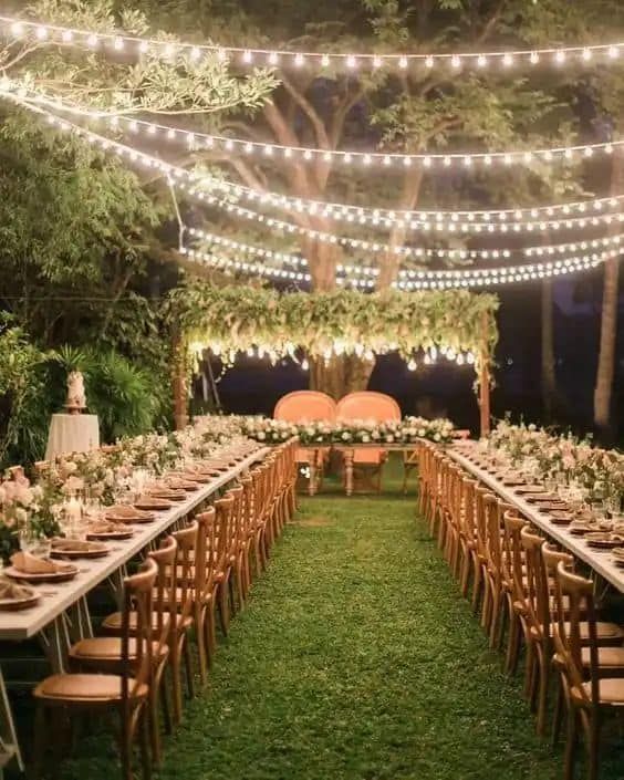 an outdoor wedding reception setup with string lights and wooden chairs, greenery and candles