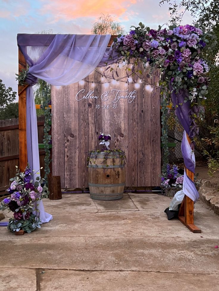 an outdoor wedding setup with purple flowers and lavender draping on the arbors