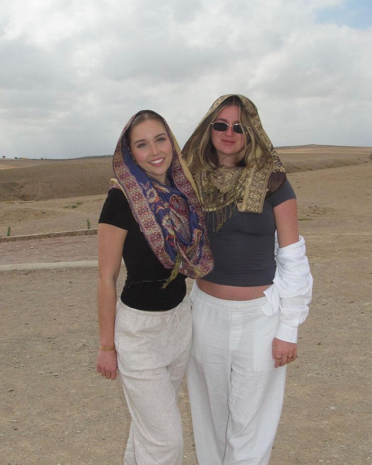 two women standing next to each other wearing white pants and scarves on their heads