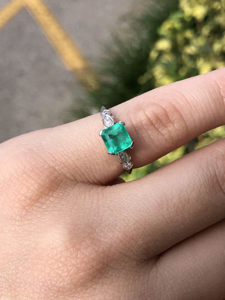 a woman's hand holding an emerald and diamond ring on top of her finger