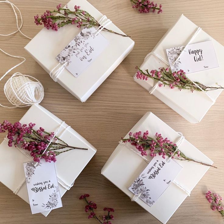 four gift boxes with flowers tied to them on top of a wooden table next to twine string