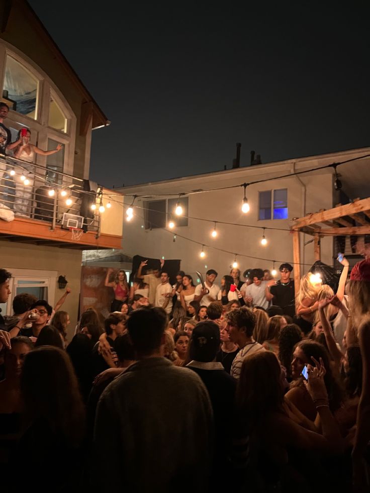 a group of people standing around each other in front of a building with lights on