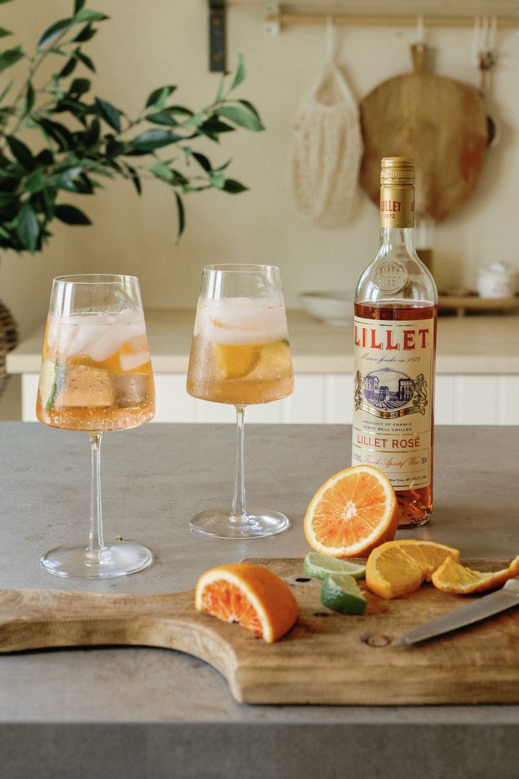 two wine glasses filled with liquid and orange slices on a cutting board