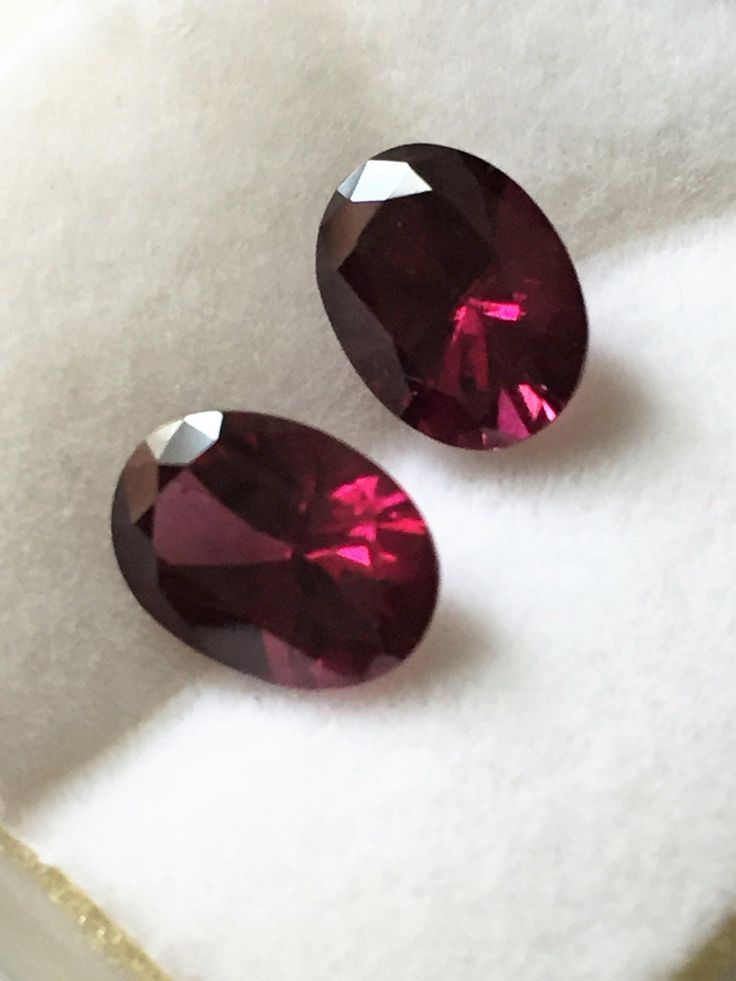 pair of pink sapphires sitting on white cloth next to gold trimmed box and paper