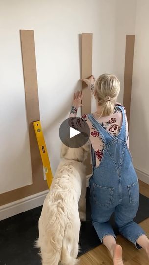 a woman in overalls is leaning against a wall with a dog on the floor