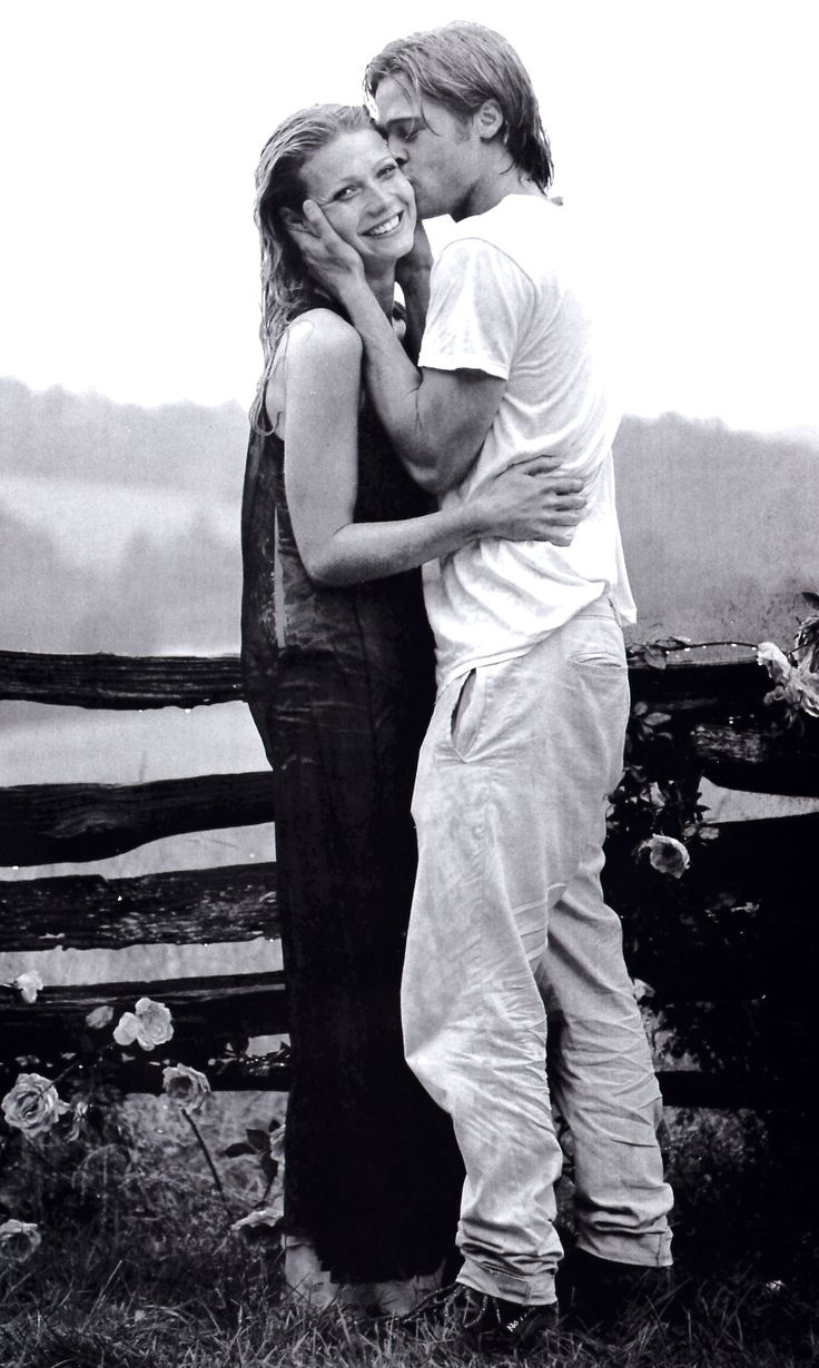 a man and woman standing next to each other in front of a fence with flowers