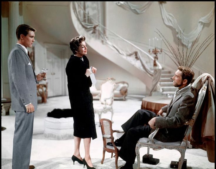 two men and a woman standing in front of a man sitting on a chair talking to each other