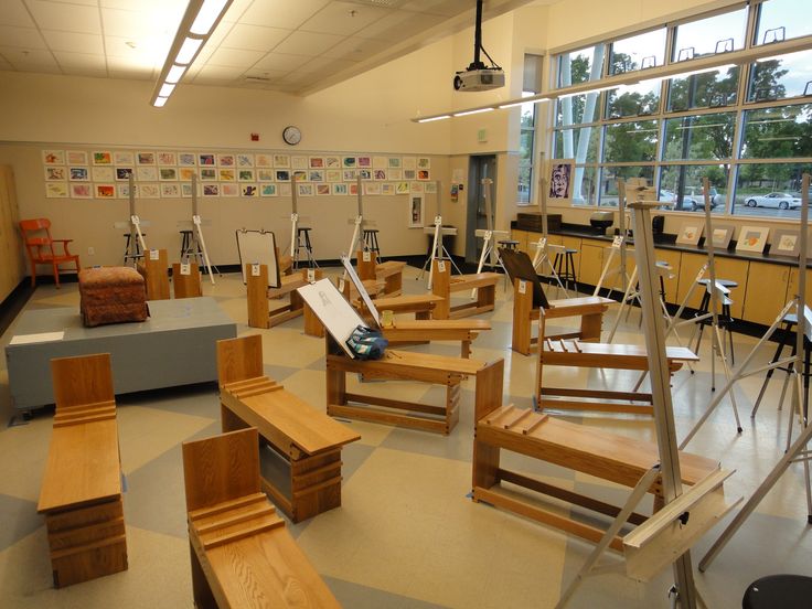 an empty classroom with wooden chairs and desks on the floor in front of large windows