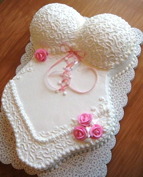 a cake shaped like a heart with pink roses on the side and two wedding rings in the middle