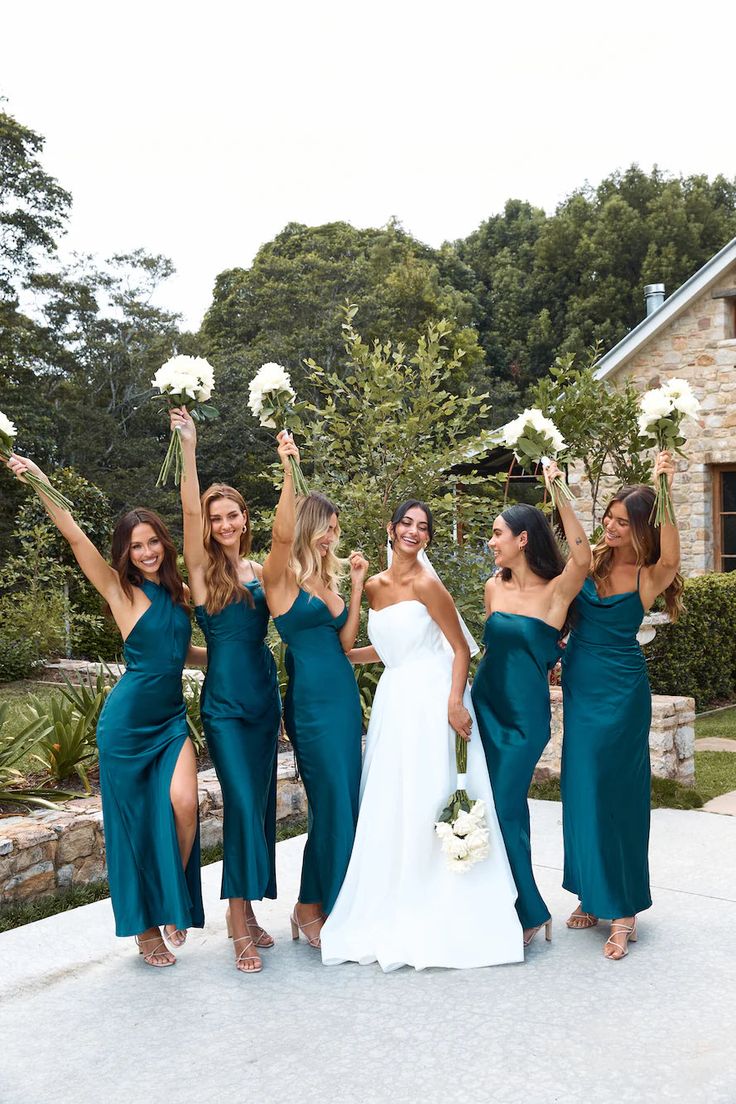 a group of women standing next to each other in front of a stone building holding bouquets