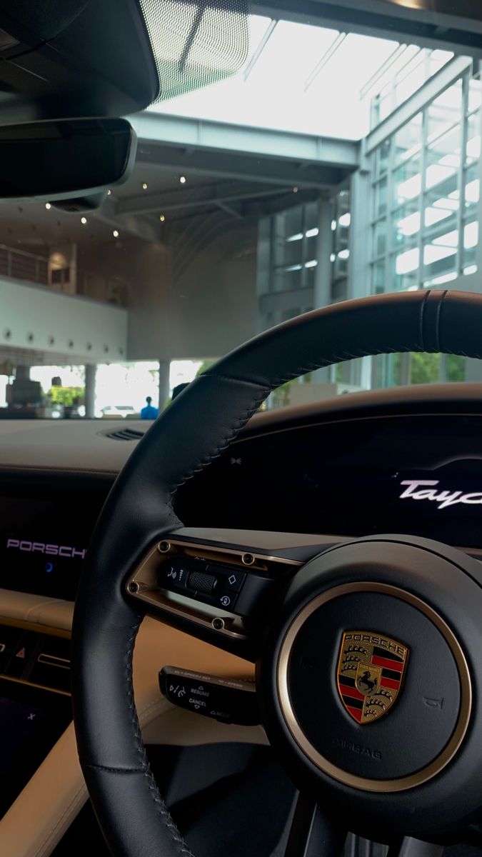 the steering wheel and dashboard of a porsche car in a showroom with large windows