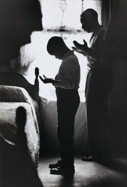 two young boys standing in front of a bed looking at something on the floor with their hands