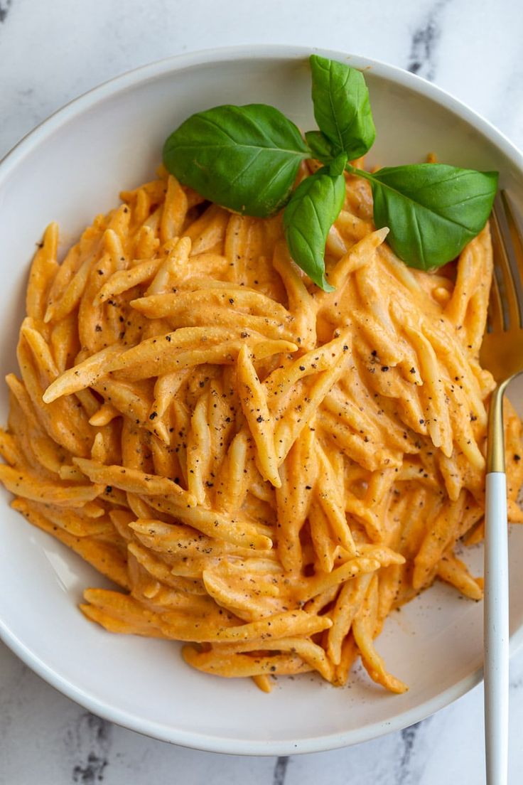 a white bowl filled with pasta and topped with basil