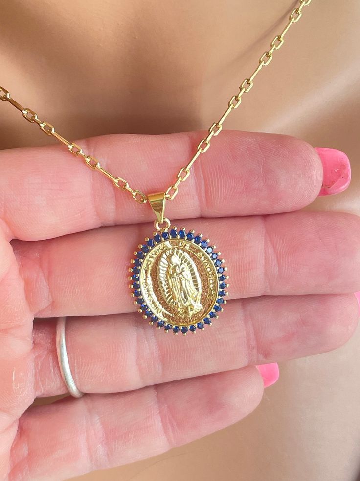 "This is a lovely 18K gold filled our Lady of Guadalupe pendant necklace. This beautiful necklace features Guadalupe image surrounded by dark blue pavé crystals. Pendant measures 24x21 and comes on this beautiful 3 to 1 link chain with spring clasp in back. Entire necklace is 18k gold filled. Model is wearing a 16\" leng.  Choose your desired length. Comes in a gift box ready to present. Please pay attention to delivery time which is stated on this listing. All my jewelry is handmade and made to Blue Medallion Necklace With Coin Pendant, Oval Our Lady Of Guadalupe Necklace For Gift, Gold Virgin Mary Medallion Jewelry, Oval Our Lady Of Guadalupe Necklace Gift, Blue Coin Pendant Jewelry For Gifts, Blue Coin Pendant Jewelry As Gift, Gold Plated Miraculous Medal Jewelry As Gift, Gold Plated Spiritual Necklace With Miraculous Medal, Spiritual Gold Plated Necklaces With Miraculous Medal