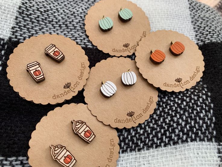 four wooden earrings are sitting on top of a plaid tablecloth with tags attached to them