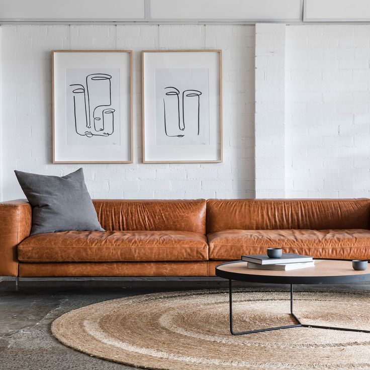 a living room with two pictures on the wall and a leather couch in front of it