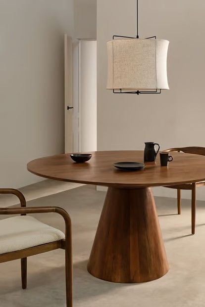 a wooden table with two chairs and a light hanging from the ceiling over it in a white room