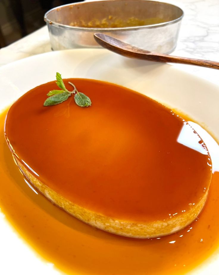 a dessert with caramel sauce on a white plate next to a silver bowl and spoon