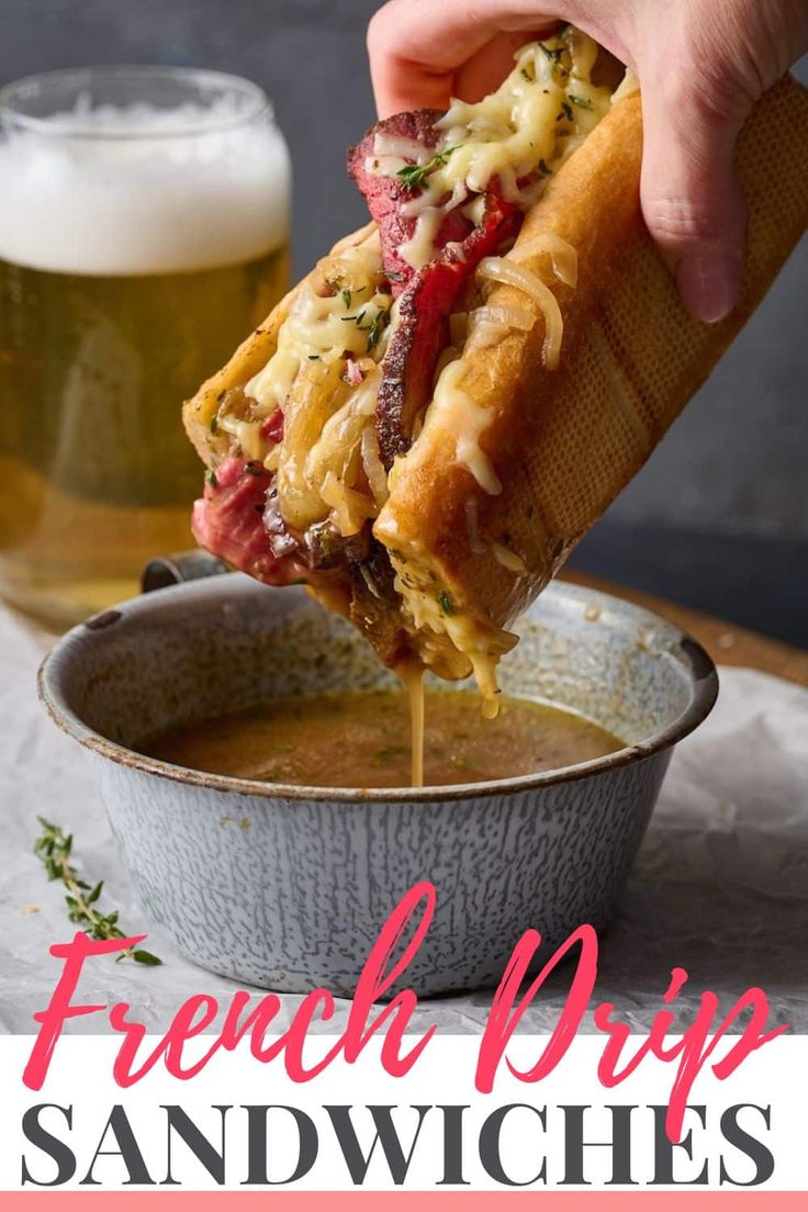 a person holding a sandwich over a bowl of soup with a beer in the background