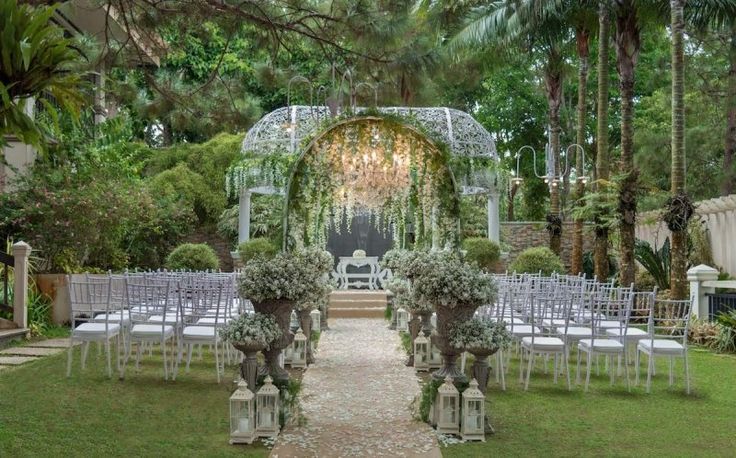 an outdoor ceremony setup with white chairs and greenery