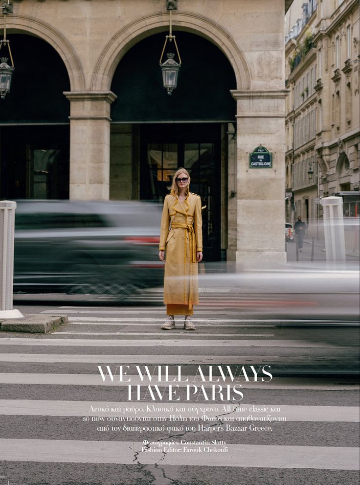 a woman in a yellow trench coat is standing on the street with cars passing by