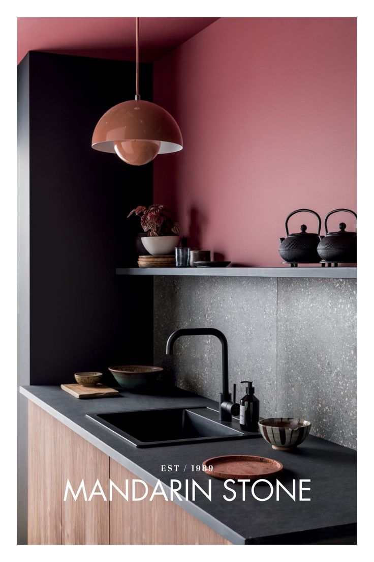 a kitchen with pink walls and black countertops, an island sink and wooden cabinets