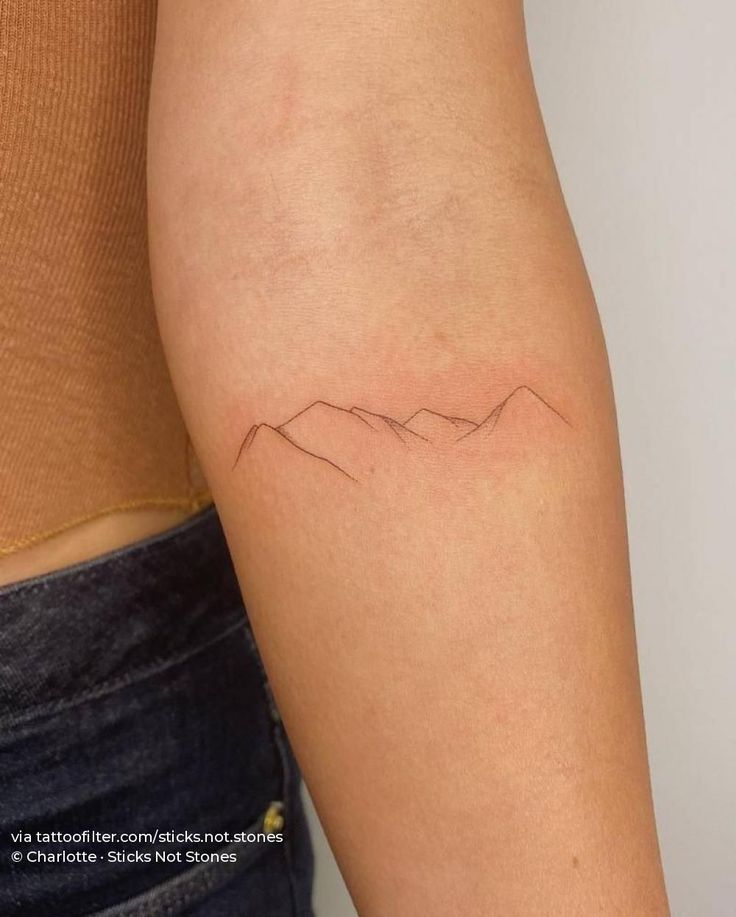 a woman's arm with a small mountain tattoo on the left side of her arm