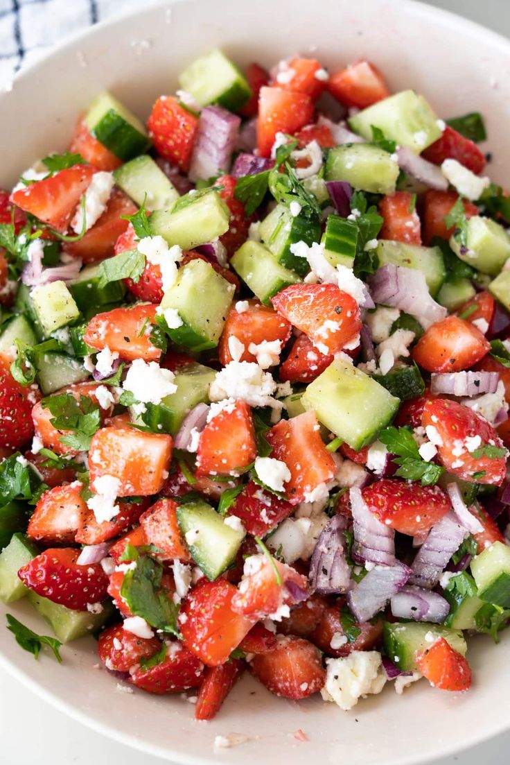 a salad with cucumbers, strawberries and feta cheese in a white bowl