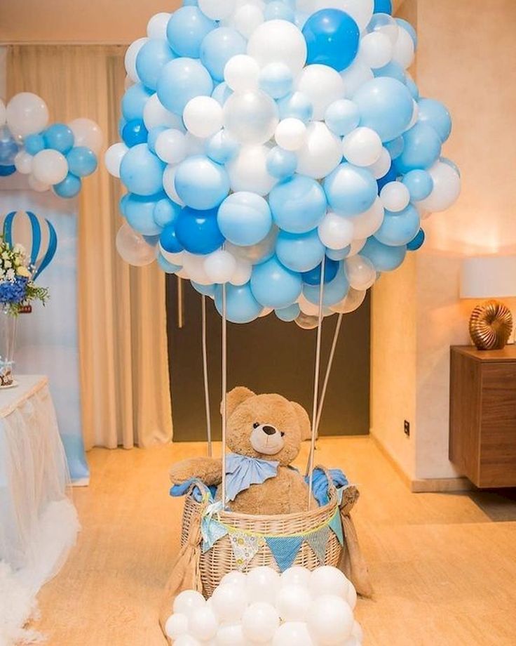 a teddy bear sitting in a basket with blue and white balloons attached to the balloon