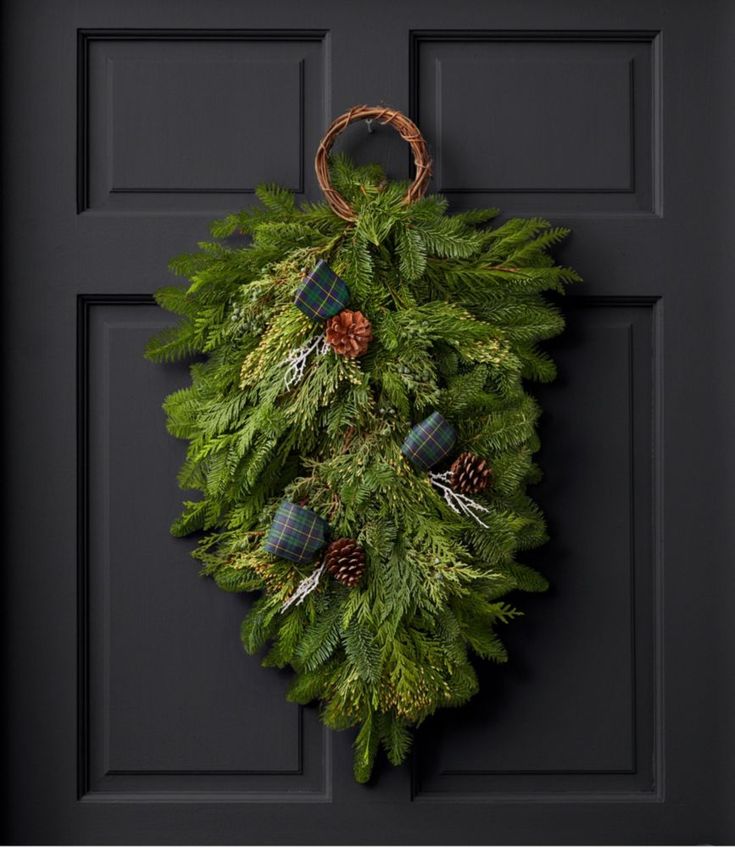 a wreath hanging on the front door with pine cones and evergreen leaves, plaid flannel