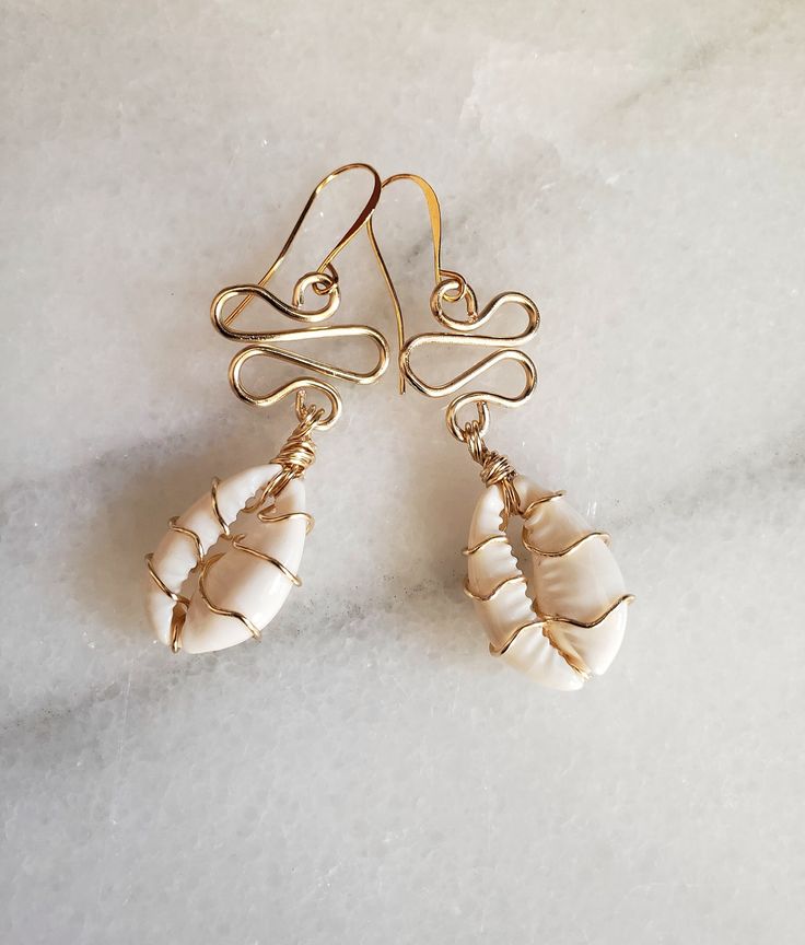 "These pretty pearl white cowrie shells are wrapped in your choice of metal wire. They are going to stand out no matter what your wearing.  Cute, earthy, lighweight and fresh. Just a funky earring for all occasions. Hangs at roughly 2\" in length. Z.A.B original." Cowrie Jewelry Ideas, Cowrie Shell Decor, Cowry Shell Jewelry, Hawaiian Shell Jewelry, Shell Earrings Diy Seashell Jewelry, Shell Earrings Diy, Diy Shell Jewelry, Shell Jewelry Ideas, Cowrie Shell Jewelry