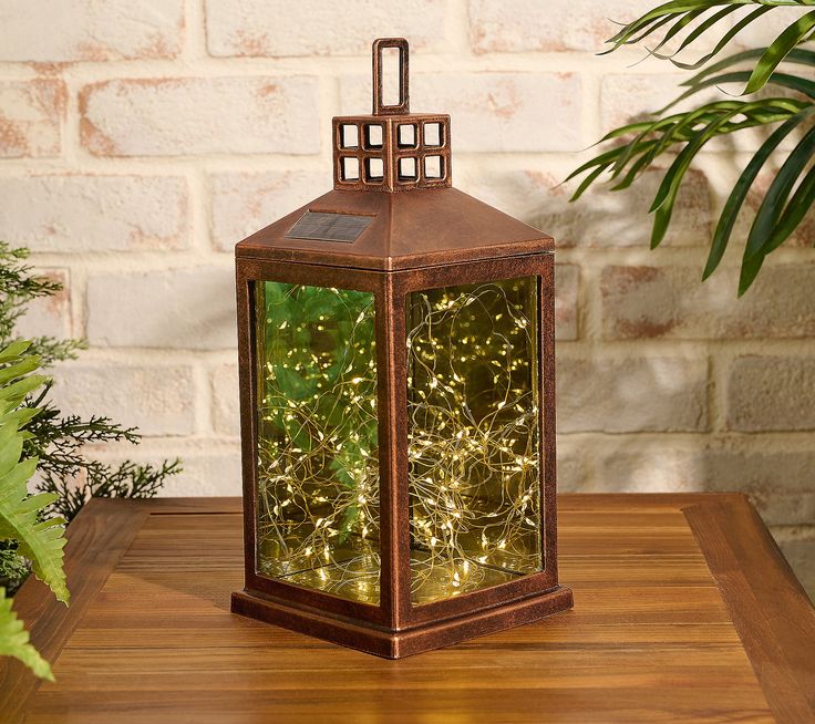 a lighted lantern sitting on top of a wooden table next to a potted plant