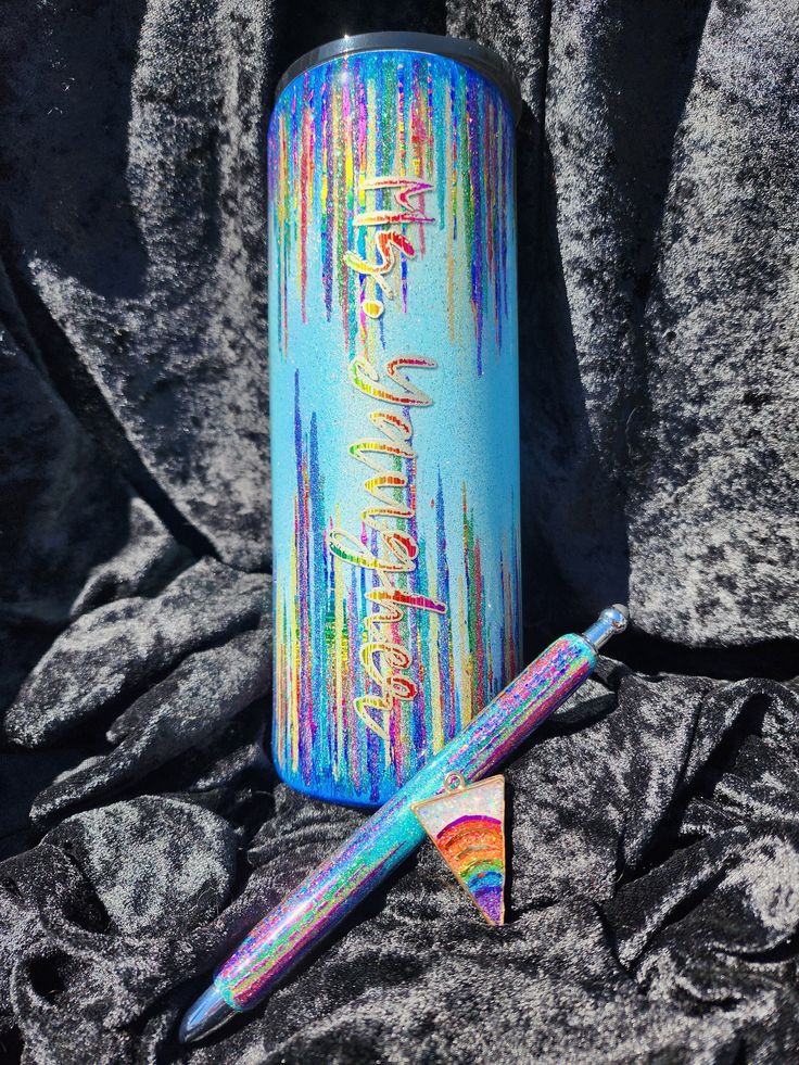 a blue spray paint can next to a rainbow fountain pen on a gray blanket with black background