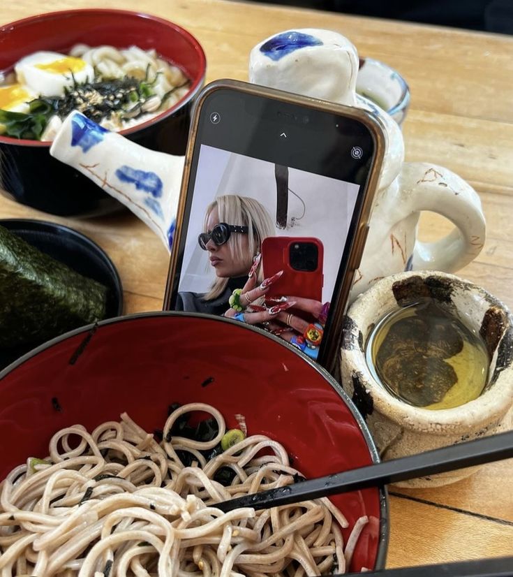 a bowl of noodles with chopsticks and a cell phone sitting on the table